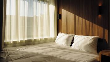 A neatly made bed with white linens, a wooden headboard, and a wall-mounted light fixture.