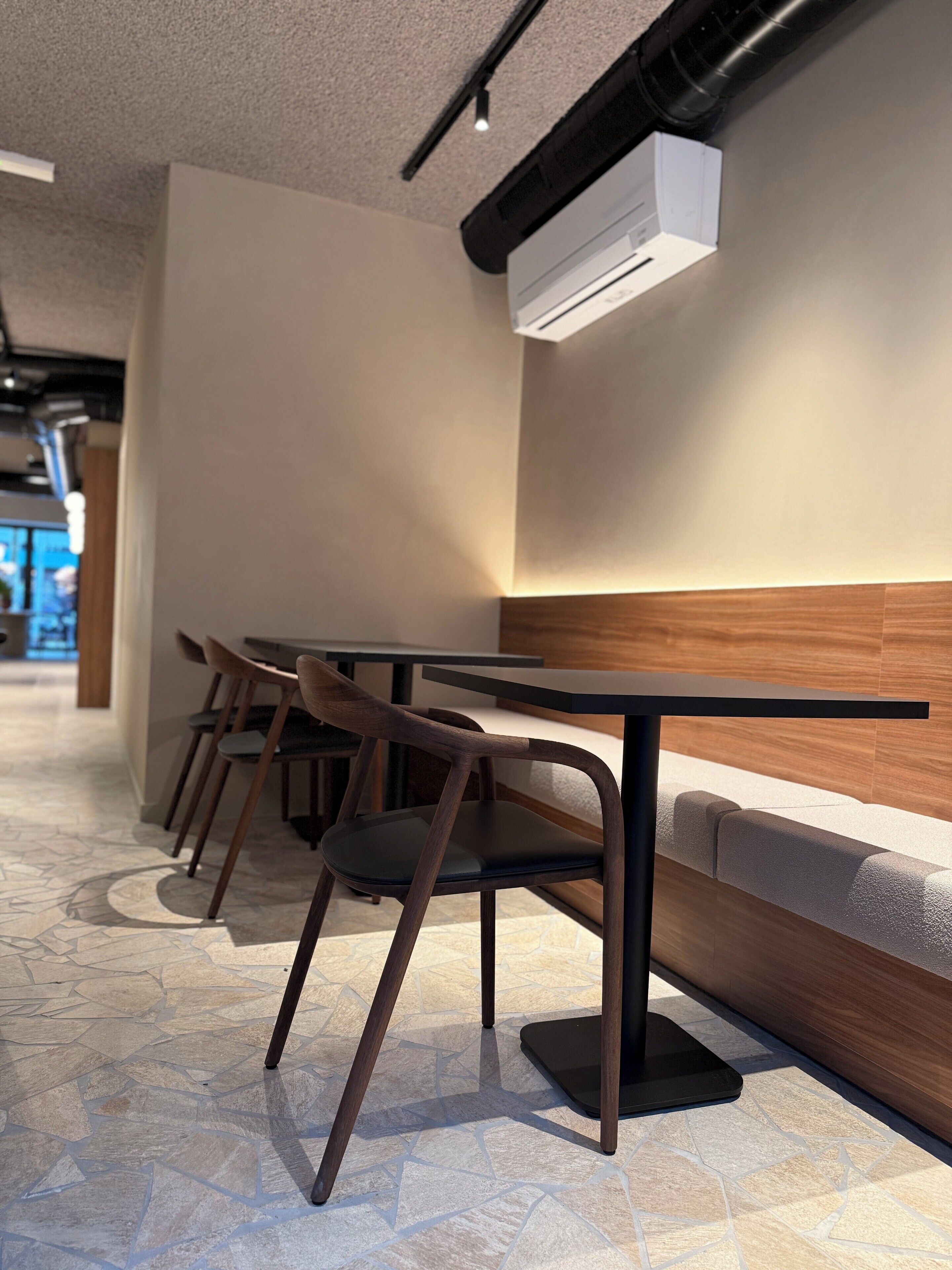 Un interior moderno con una fila de mesas y sillas de madera, un suelo estampado y un equipo de aire acondicionado instalado en la pared.