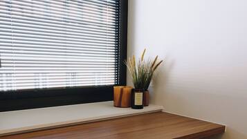 Een houten bureau met een stoel, een raam met zonwering en een bloempot op de vensterbank.