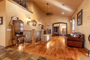 Amplia sala de estar con piso de madera, un sofá de cuero y una escalera con una rueda decorativa.