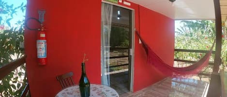 Ein rotes Zimmer mit Glastür, Feuerlöscher, einer Hängematte und einem Tisch mit einer Flasche.