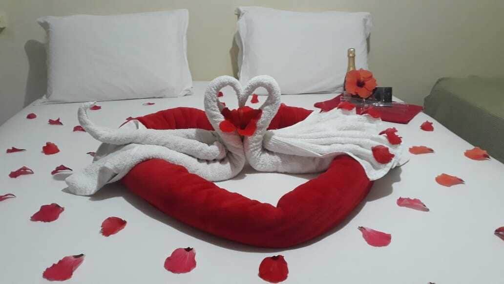 Ein Bett mit einer herzförmigen Handtuchgestaltung, roten Rosenblättern und einer Champagnerflasche.