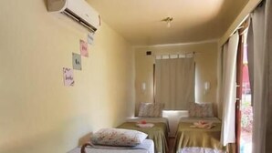 Een kamer met twee eenpersoonsbedden, een airconditioningapparaat aan de muur en een raam met gordijnen.