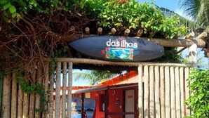 Een houten poort met een bord waarop ‘das ilhas’ staat, leidt naar een gebouw met een rood dak en een zichtbaar zwembad.