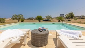 A poolside area with lounge chairs and a wicker table, a clear blue sky, and a distant view of a building labeled "medrur". - Villa Serenella - Carovigno (Carovigno)