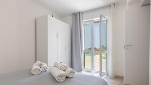 A hotel room with a bed, a wardrobe, and a door leading to a balcony with a pool view. - Villa Serenella - Carovigno (Carovigno)
