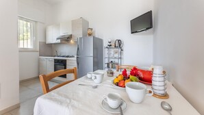 A modern kitchen with white cabinets, a grey refrigerator, and a dining table set with cups, bowls, and a fruit bowl. - Villa Serenella - Carovigno (Carovigno)
