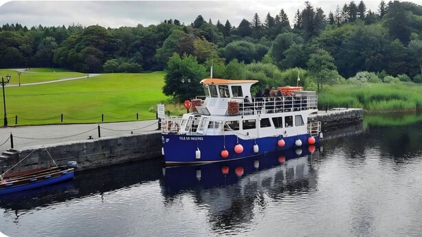 A boat docked at a pier with a grassy area and trees in the background. - House on the Lane, in the tranquil Village of Cong, Ireland. (MO)