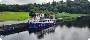 A boat docked at a pier with a grassy area and trees in the background. - House on the Lane, in the tranquil Village of Cong, Ireland. (MO)