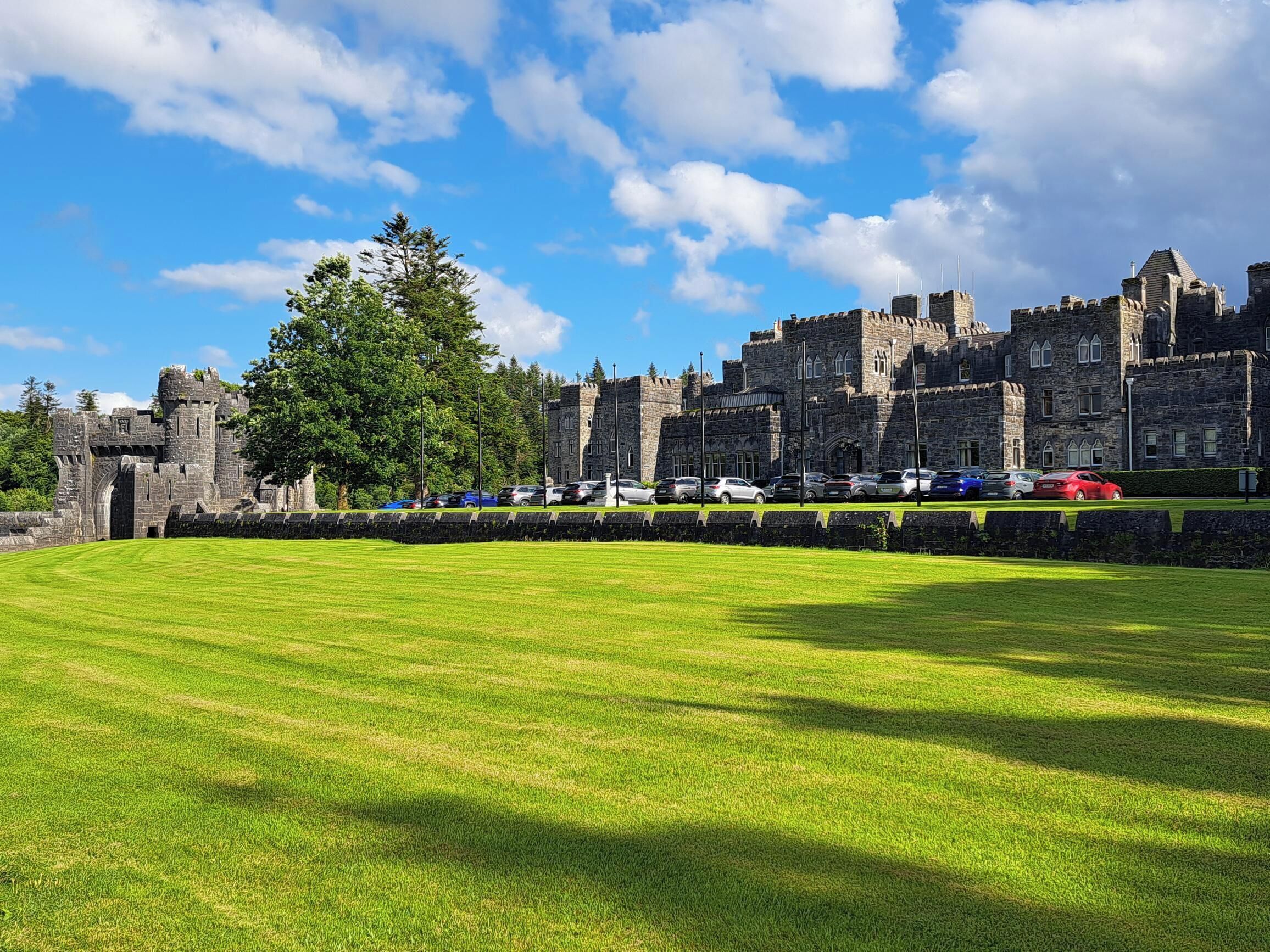 A castle with a grassy lawn in the foreground and parked cars in the background.