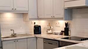 A modern kitchen with white cabinets, a marble countertop, and a built-in dishwasher. - House on the Lane, in the tranquil Village of Cong, Ireland. (MO)