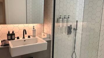 A modern bathroom with a glass-enclosed shower, a white sink with a mirror above it, and hexagonal patterned tiles.