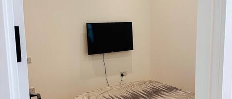 Un dormitorio con una cama, un televisor montado en la pared y suelo de madera.