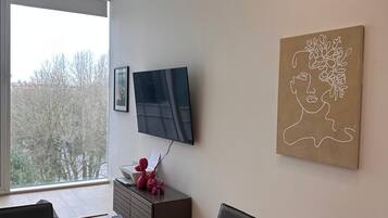 Ein modernes Wohnzimmer mit Fernseher, Esstisch und großem Fenster.