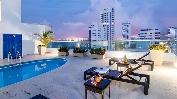 A rooftop pool area with a view of city buildings, lounge chairs, and potted plants. - Edificio Orange Castillogrande (Cartagena)