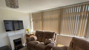 Ein Wohnzimmer mit einer Couch, einem Kamin, einem Fernseher und einem Fenster mit Jalousien.