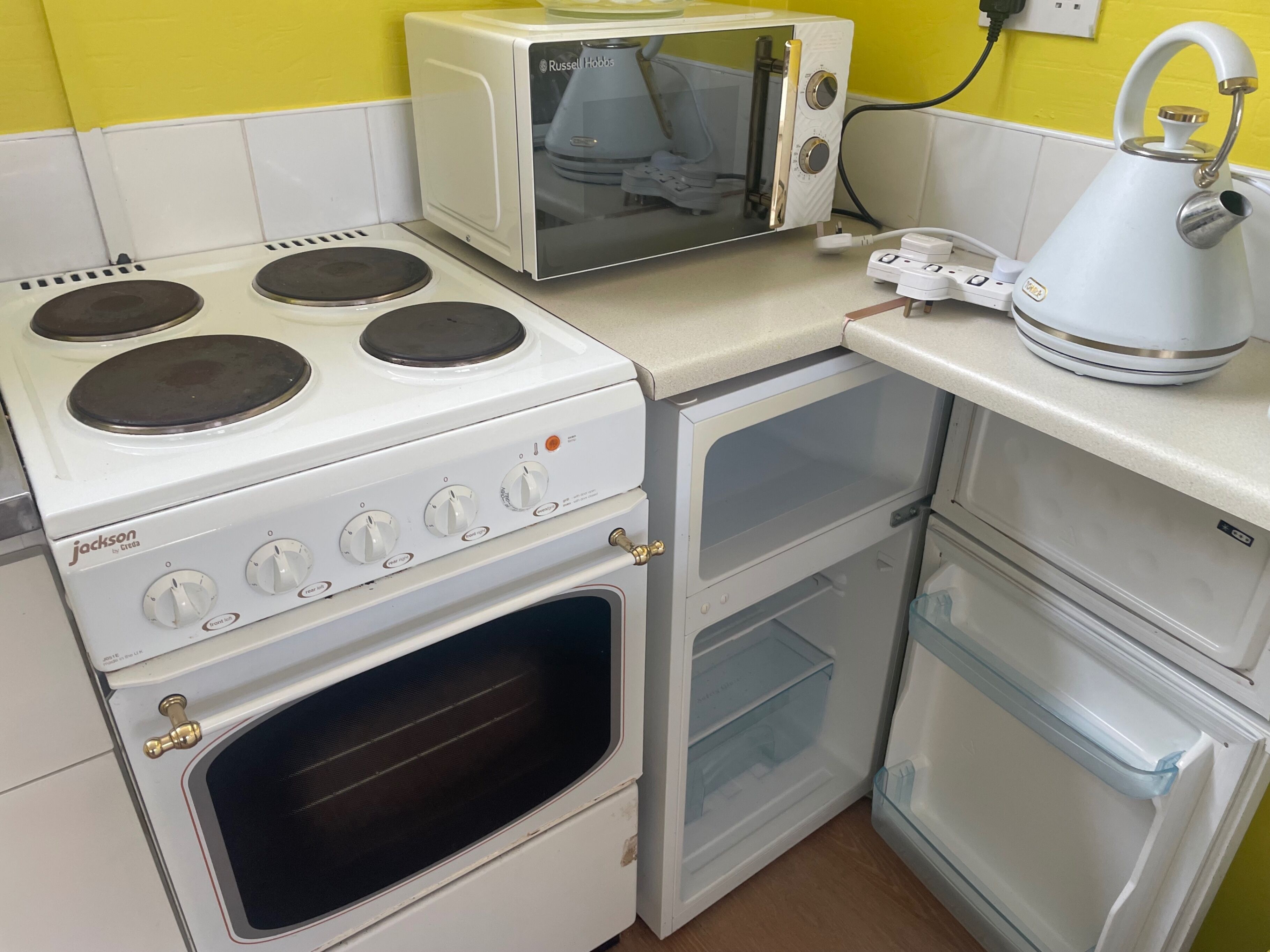 A compact kitchenette with a stove, oven, microwave, and kettle.
