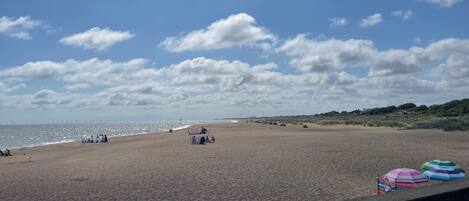 A beach with a clear sky, a few umbrellas, and a distant view of the sea.