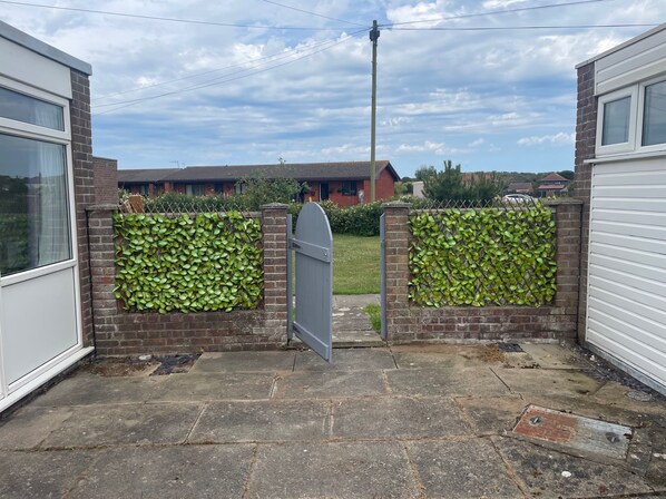 A gated entrance with a brick wall covered in green foliage, leading to a residential area with houses and a grassy lawn. - 2 Bed Lodge Sleeps 4- Pets, Parking, 2min to Beach (Skegness)