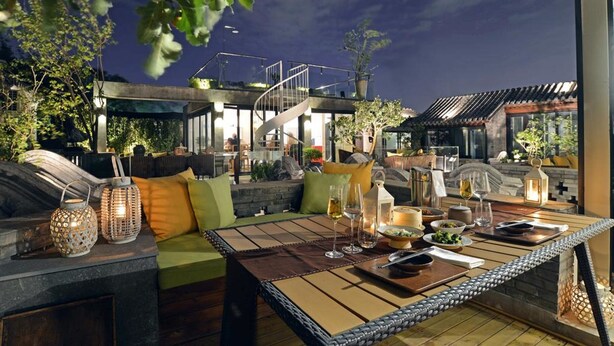 An outdoor dining area with a table set for two, surrounded by cushioned seating and decorative lanterns. - Beijing 161 Lezai Nanluo Hotel (Beijing)