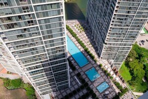 A high-rise building with a rooftop pool surrounded by greenery and other buildings.