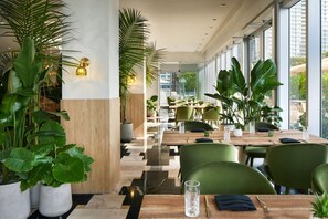 A modern restaurant interior with high ceilings, large windows, and green chairs.