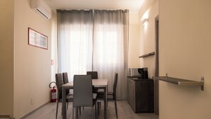 A compact room with a dining table, chairs, a small kitchenette, and a fire extinguisher. - Affittacamere Poerio (Pisa)