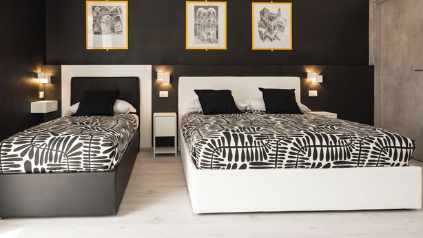 A modern bedroom with two beds, black and white patterned bedding, wall-mounted artwork, and bedside lamps. - Affittacamere Poerio (Pisa)