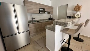 Una cocina moderna con electrodomésticos de acero inoxidable, armarios de madera, encimera de granito y una zona de bar con dos taburetes.