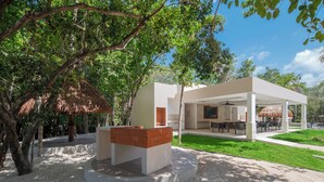 Un espacio moderno para comer al aire libre con jardinera de ladrillo, asientos cubiertos y estructura de techo de paja.