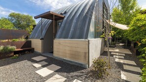 A modern greenhouse with a curved metal roof, a wooden bench, and a gravel pathway.