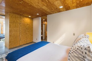 Camera da letto con soffitto in legno, letto con copriletto a motivi e un piccolo tappeto decorativo blu.