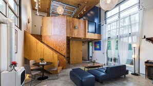 A modern interior with a loft-style staircase, a sofa, a dining area, and a large window providing natural light.