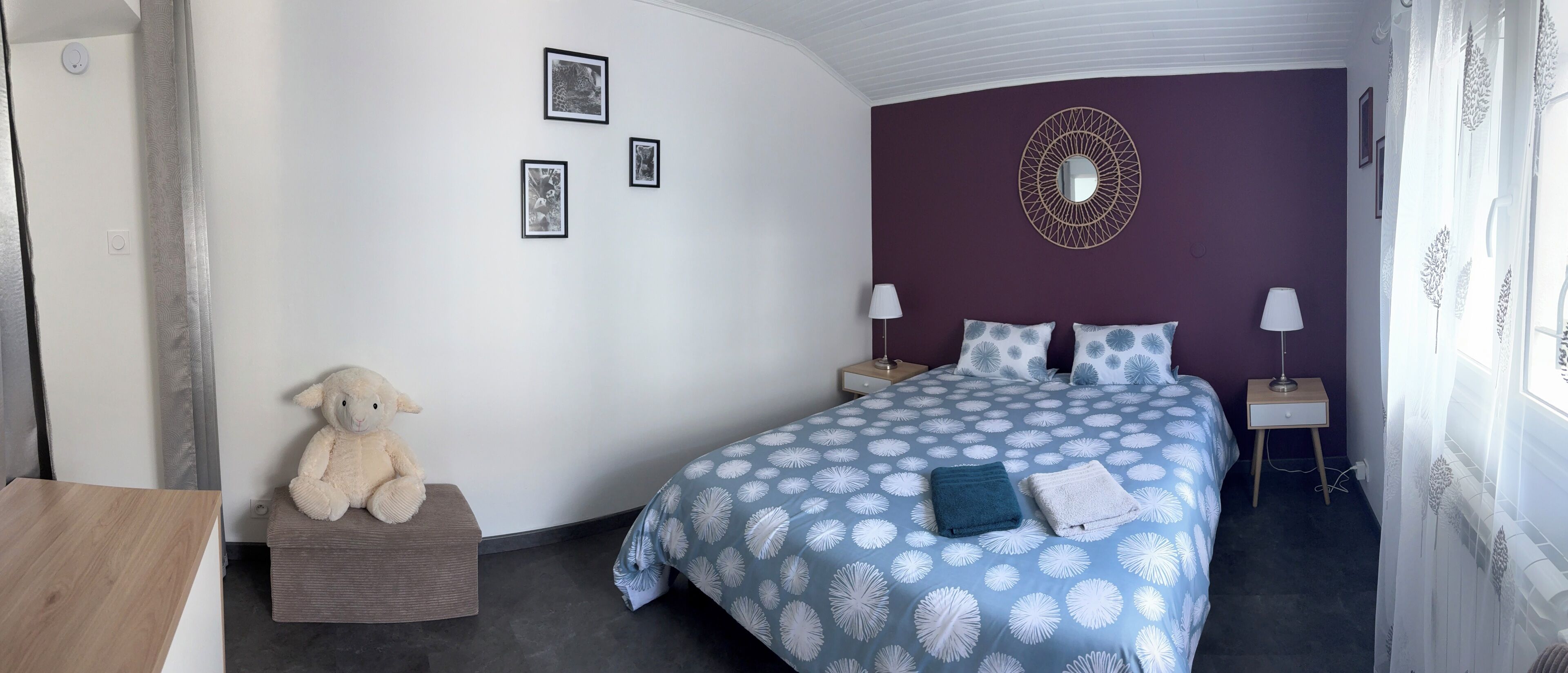 A bedroom with a bed, two nightstands, a lamp, a wall-mounted mirror, and a stuffed animal on a bench.