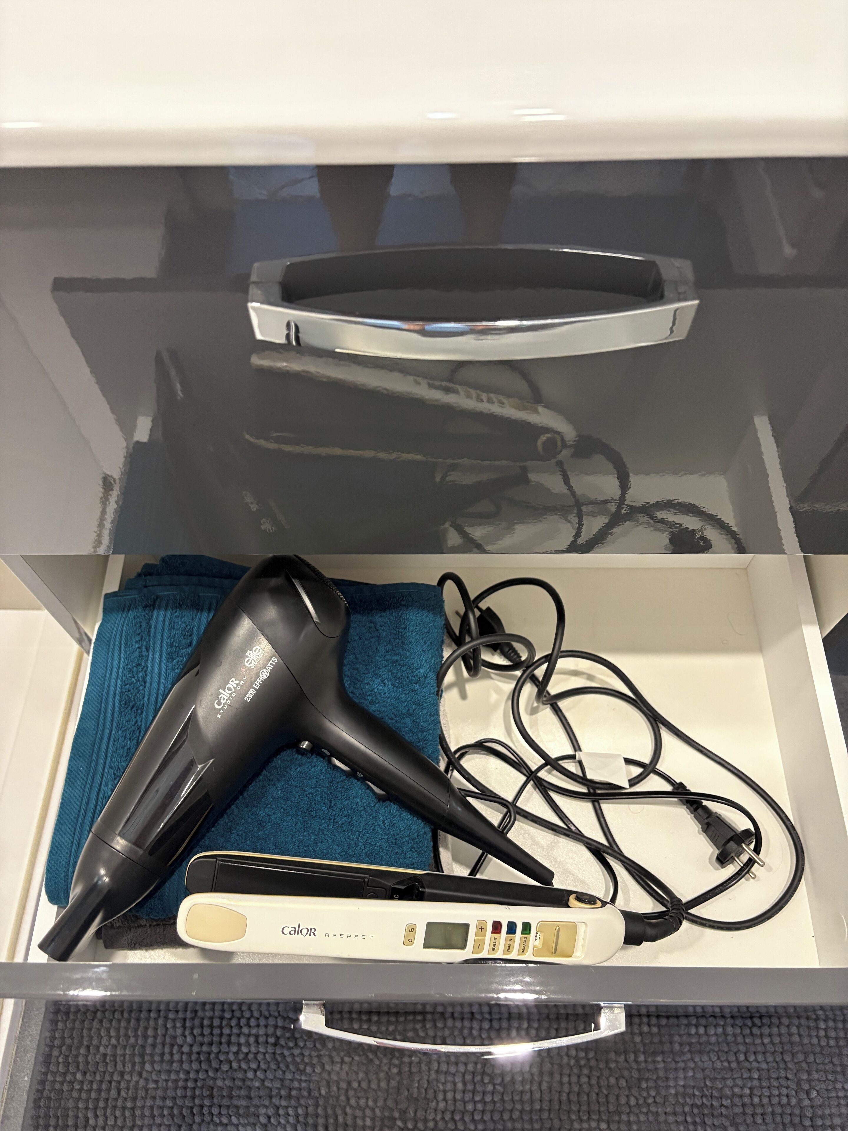 Eine Schublade mit einem Haartrockner, einem blauen Handtuch und einem Glätteisen mit digitaler Anzeige.