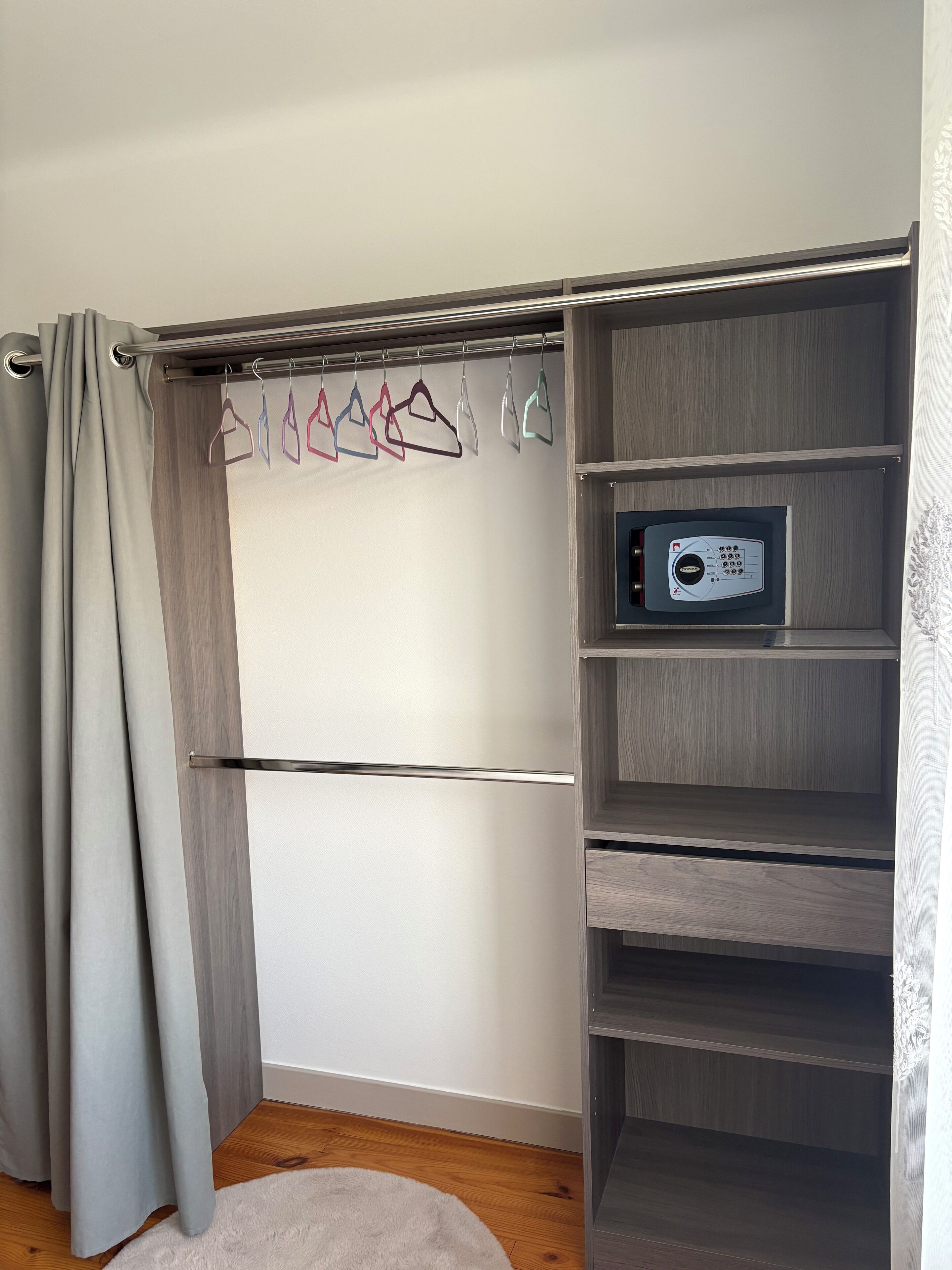 Ein moderner Kleiderschrank mit grauen Vorhängen, einer Kleiderstange und einem Bedienfeld auf der rechten Seite.