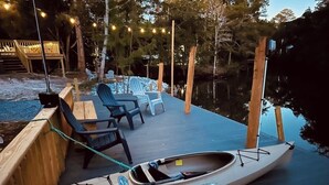 Un muelle de madera con una canoa y sillas, rodeado de árboles y luces colgantes.