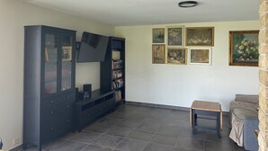 A living room with a dark wooden entertainment unit, a flat-screen TV, a small wooden table, and a sofa. There are six framed artworks on the wall. - Bell Air near Neuchatel (Val-de-Ruz)