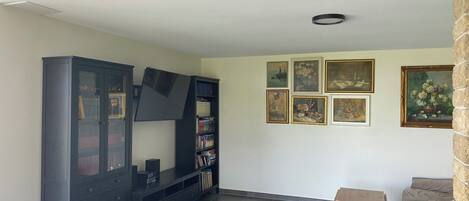 Una sala de estar con un mueble de entretenimiento de madera oscura, un televisor de pantalla plana, una mesita de madera y un sofá. Hay seis obras de arte enmarcadas en la pared.
