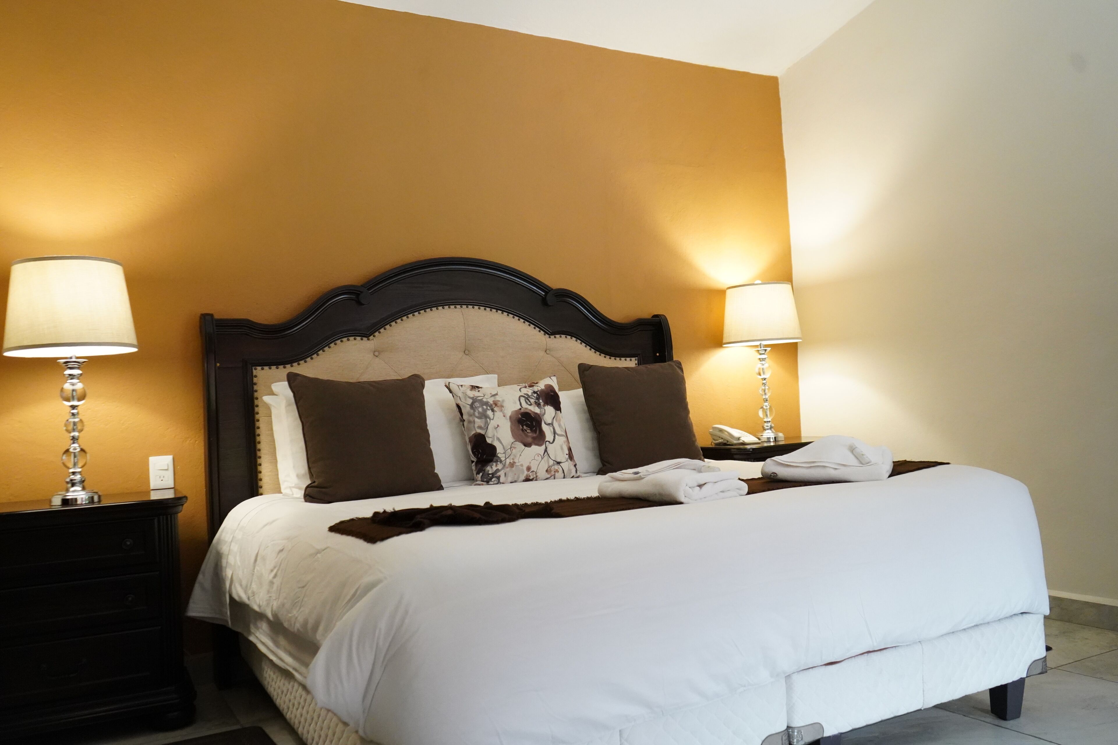 A neatly made bed with white bedding, two bedside lamps, and a floral pillow.