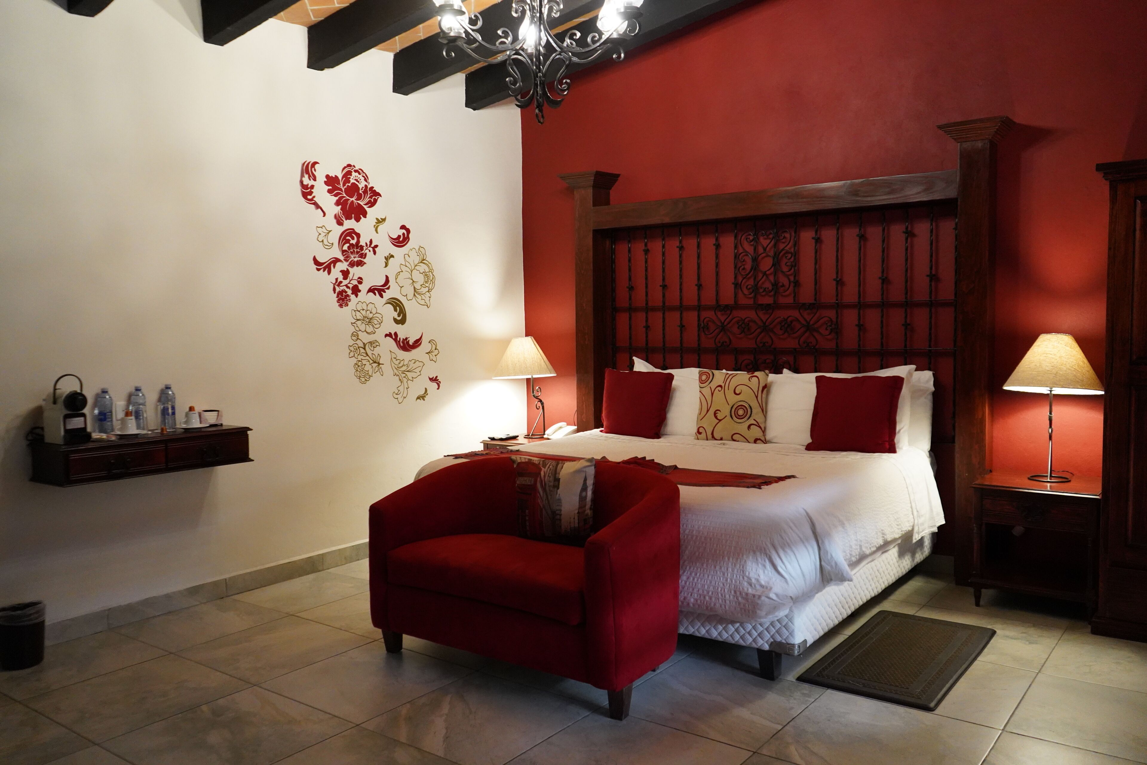 A hotel room with a large bed, two bedside lamps, a red armchair, a wall with floral decals, and a wooden headboard.