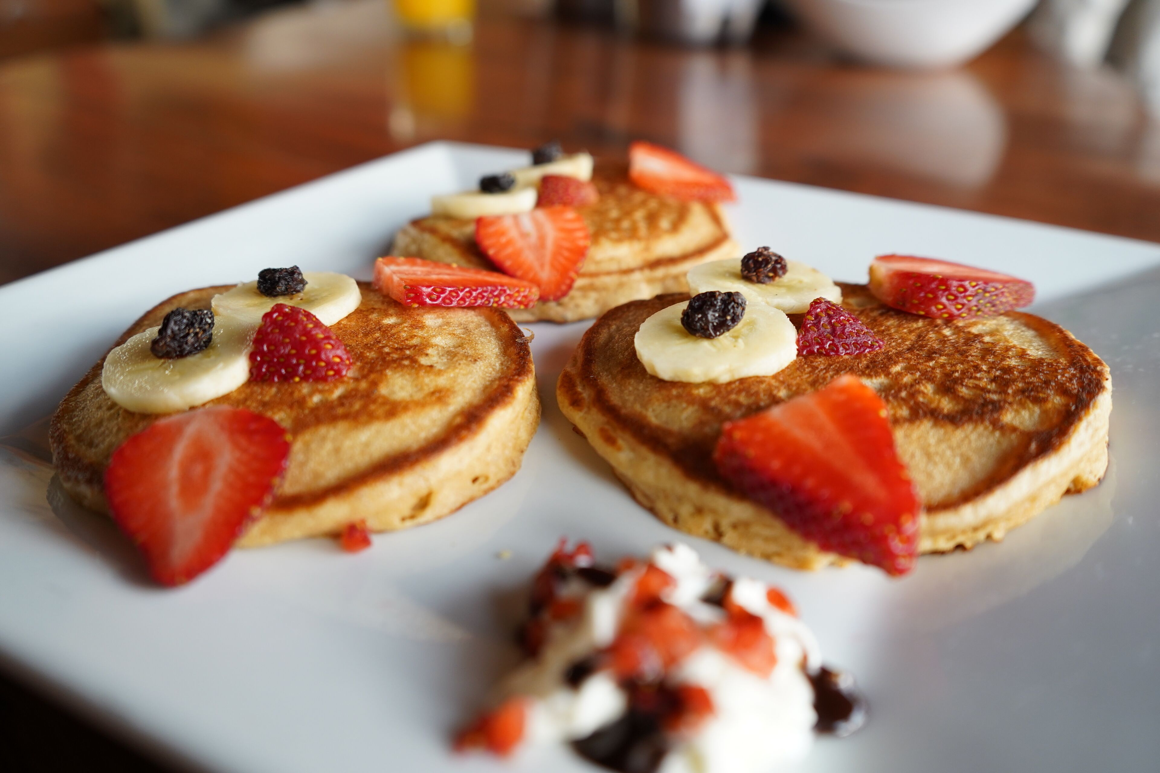 Three pancakes topped with strawberries, bananas, and blueberries on a white plate.