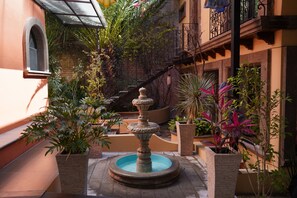 Un patio con una fuente central, rodeado de macetas y una escalera de ladrillo.