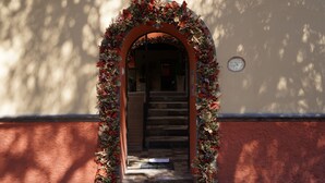 Une entrée en arc surmontée d’une guirlande de fleurs, un escalier menant à l’intérieur et une enseigne fixée au mur.