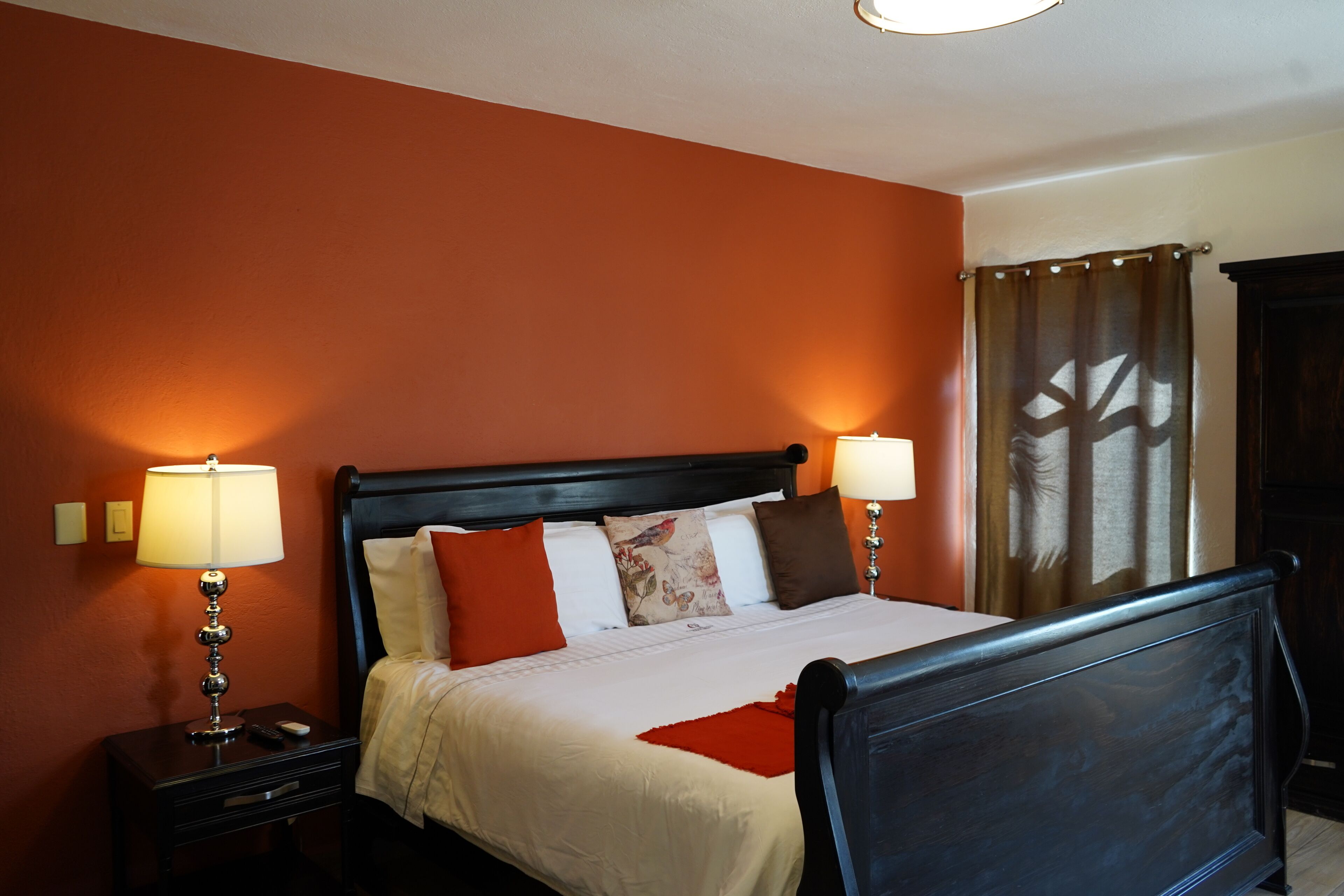 A hotel room with a bed, two bedside tables, a nightstand, a lamp, and a curtain.