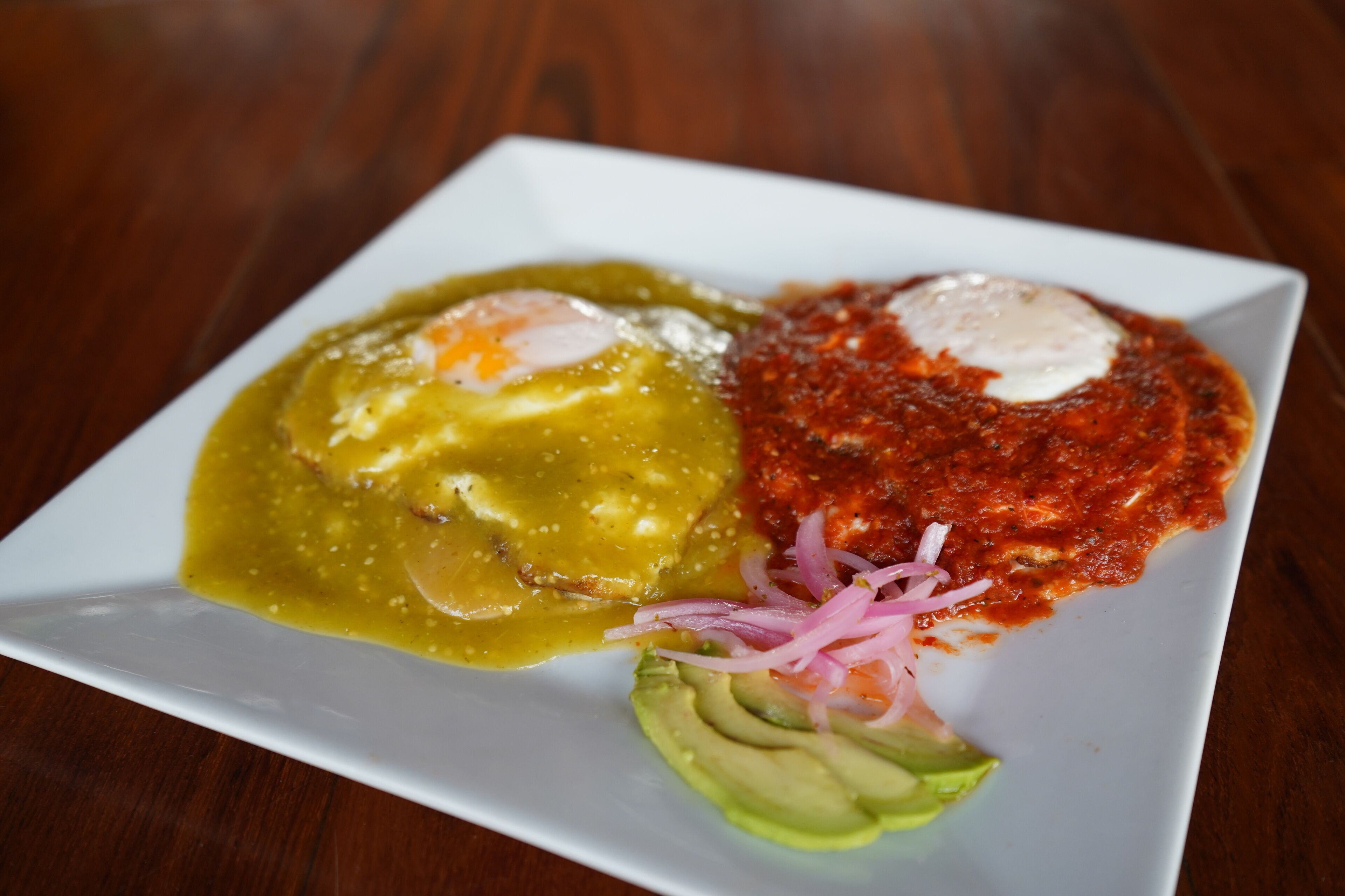 A plate with a poached egg, avocado slices, and a red sauce with onions.