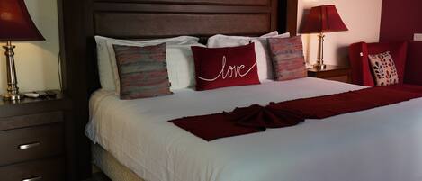 Una cama bien hecha con sábanas blancas y un plaid rojo, rodeada de almohadas decorativas, incluyendo una con la palabra 'love'.