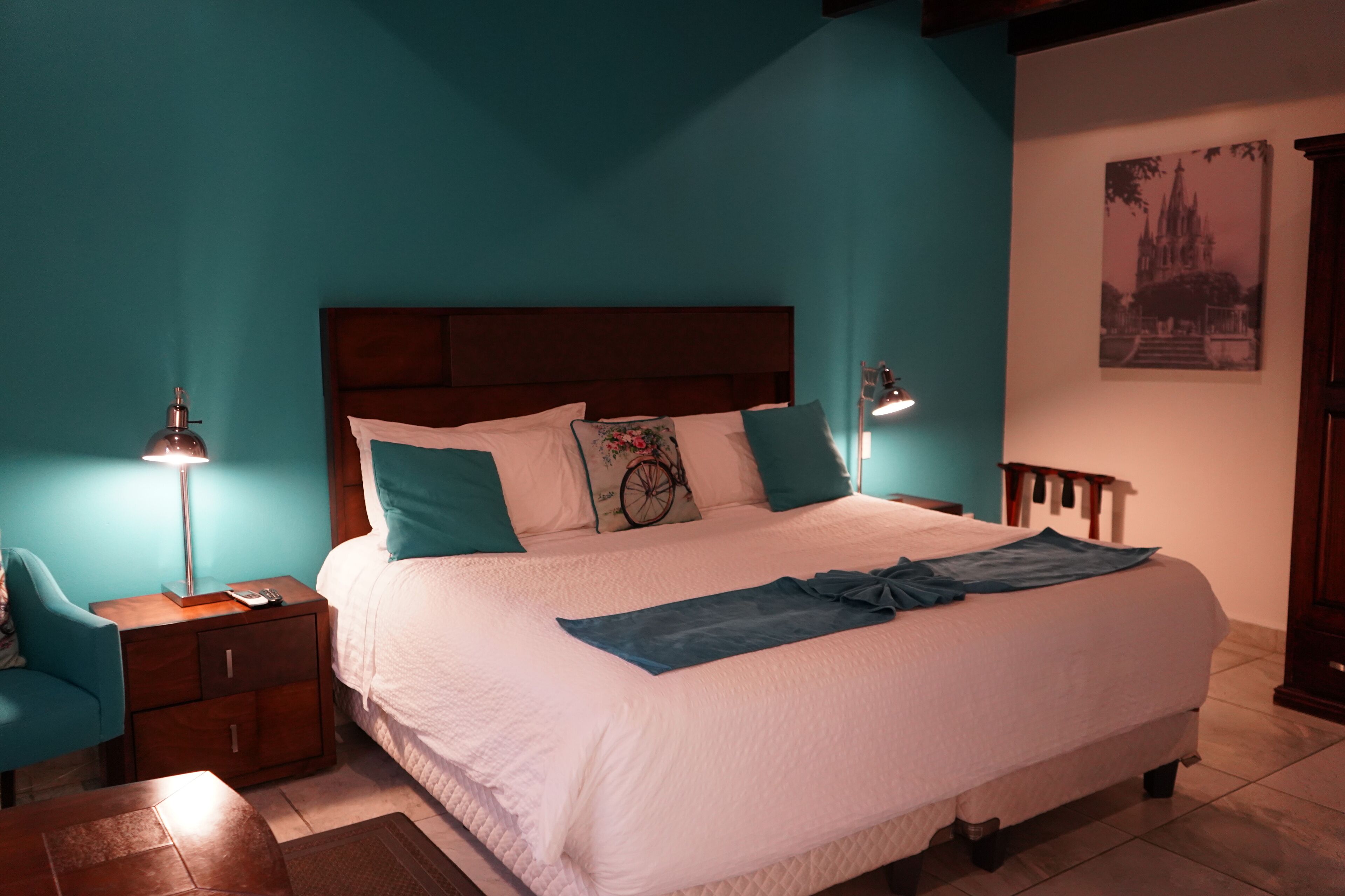 Ein ordentlich bezogenes Bett mit blauer Decke, einem hölzernen Kopfteil und teal-farbenen Wänden.