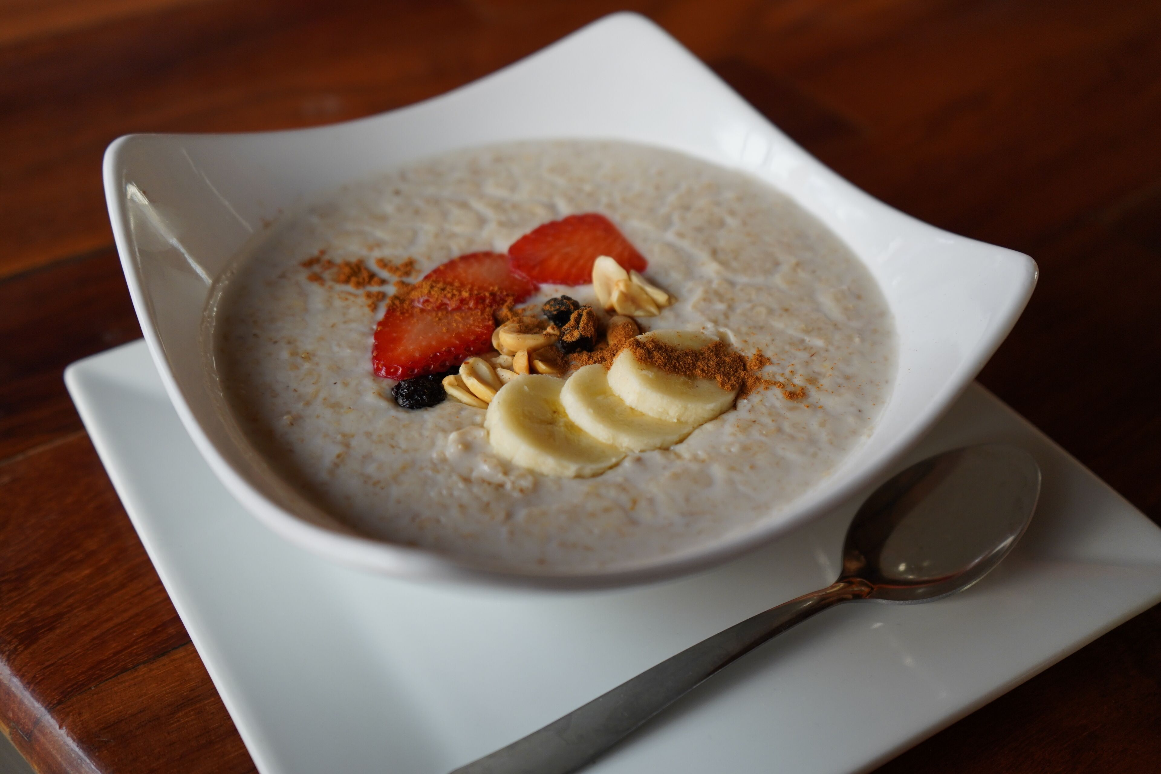Un tazón de avena con fresas, rodajas de plátano y nueces sobre un plato blanco con una cuchara.