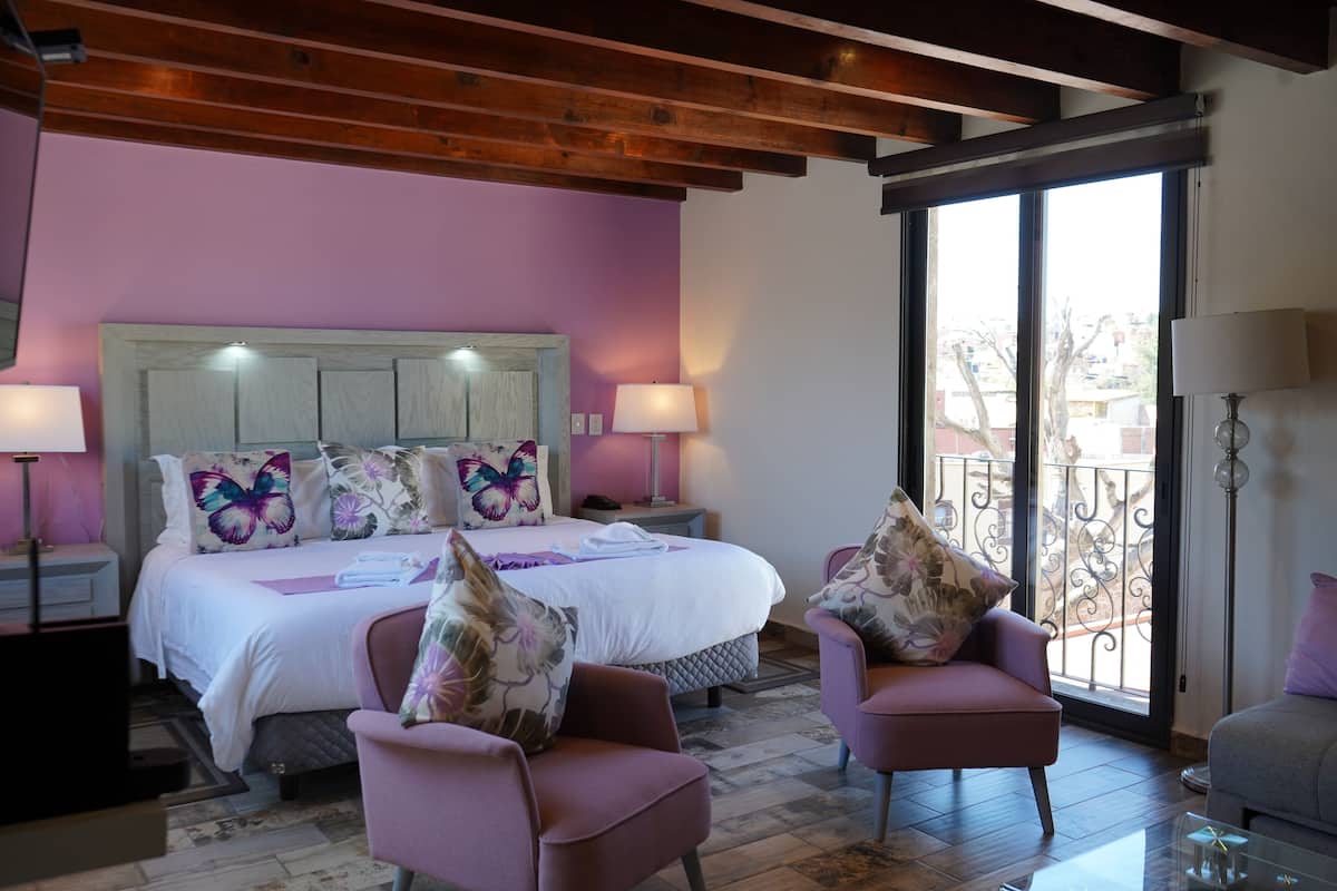 Quarto com cama, duas cadeiras, mesa de cabeceira e janela com vista.